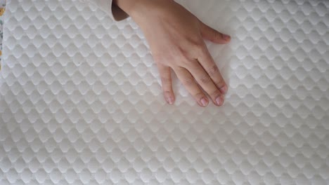 close-up of a person's hand touching a soft, white quilted mattress