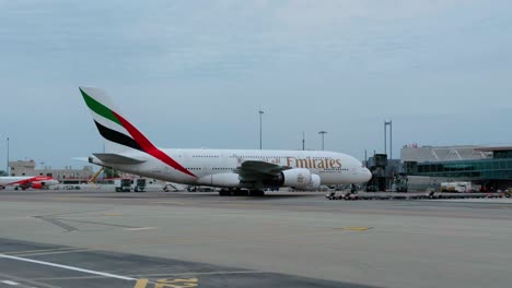 emirates plane arriving at jet bridge at nice airport terminal gate. slow pan right