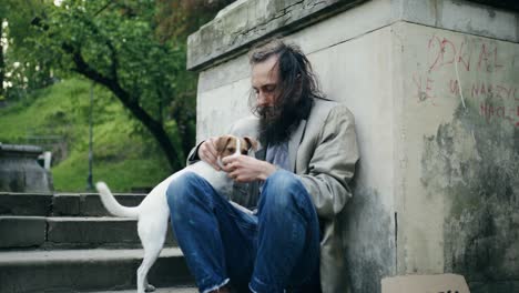 Middle-aged-dirty-homeless-man-sitting-by-the-steps-cuddling-his-dog