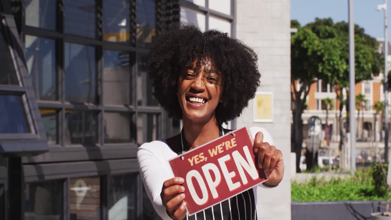 Happy african american female cafe worker showing were open signage and smiling