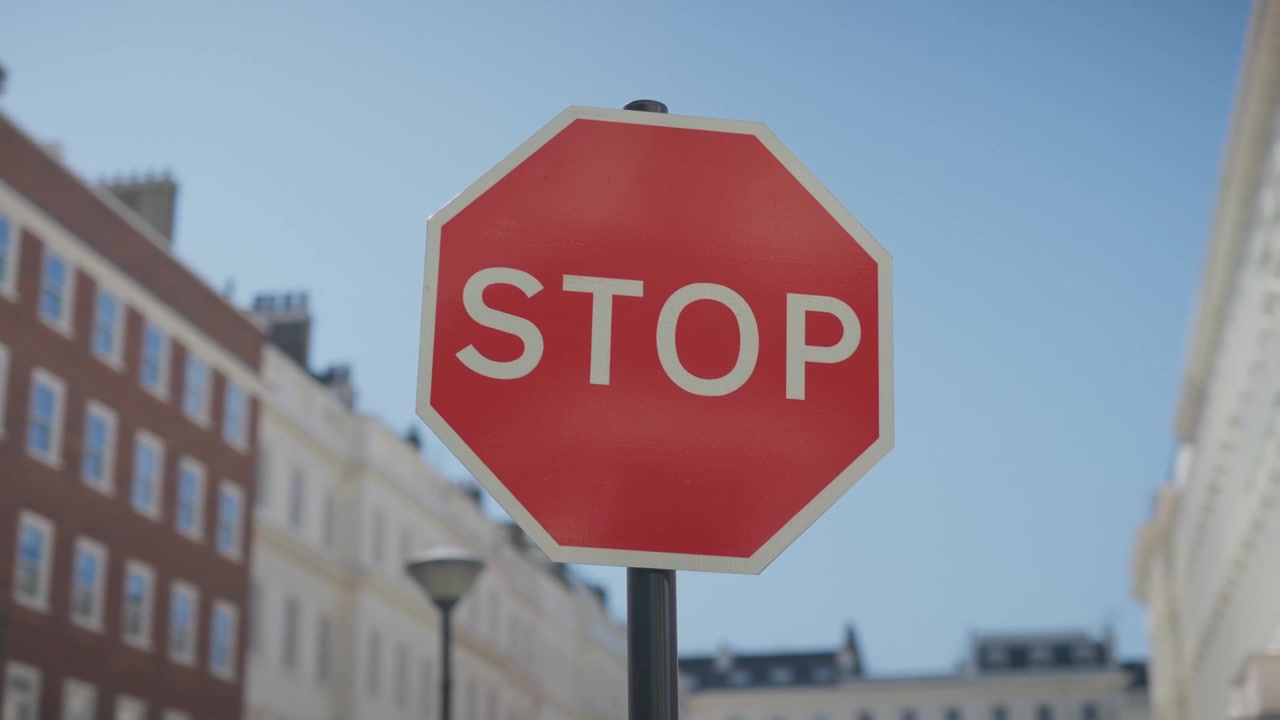 Kinematisk nærbilde av et klassisk London stoppskilt på en rolig, eksklusiv gate. Grunn dybdeskarphet med mykt uskarp London-arkitektur i bakgrunnen, stemningsfullt overskyet lys, subtilt regn