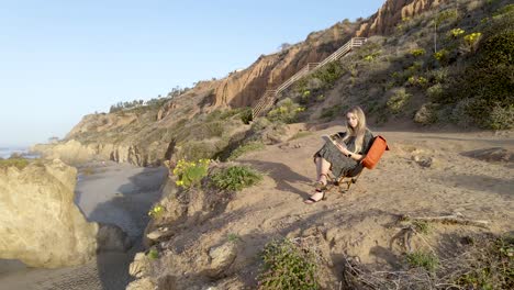 Young-caucasian-girl-reads-book-sitting-on-cliff-over-El-Matador-beach,-California