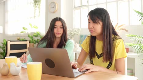 two women working on a laptop at a table indoors