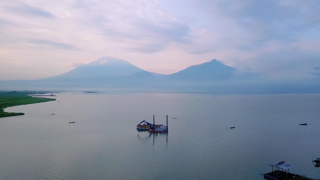 vista aérea del barco dragador con excavadora en el lago para limpiar basura y raspar barro con vista a la montaña en el fondo - lago rawa pening, indonesia