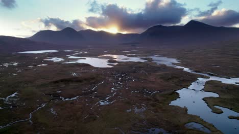 Un-Dron-Desciende-Lentamente-Hacia-Un-Paisaje-De-Humedales-De-Islas-Y-Turberas-Rodeadas-De-Agua-Dulce-Mientras-Mira-Hacia-Las-Montañas-Oscuras-Al-Atardecer