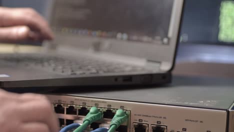 Network engineer typing and connecting Ethernet cables to switch