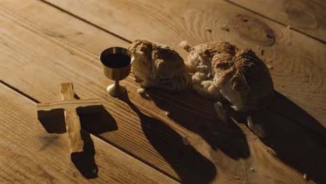 concepto religioso filmado con cáliz cruz de pan roto y vino en una mesa de madera con un charco de luz