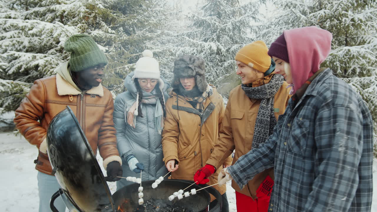 친구들이 겨울 숲에서 불에 마쉬멜로를 고 있습니다.