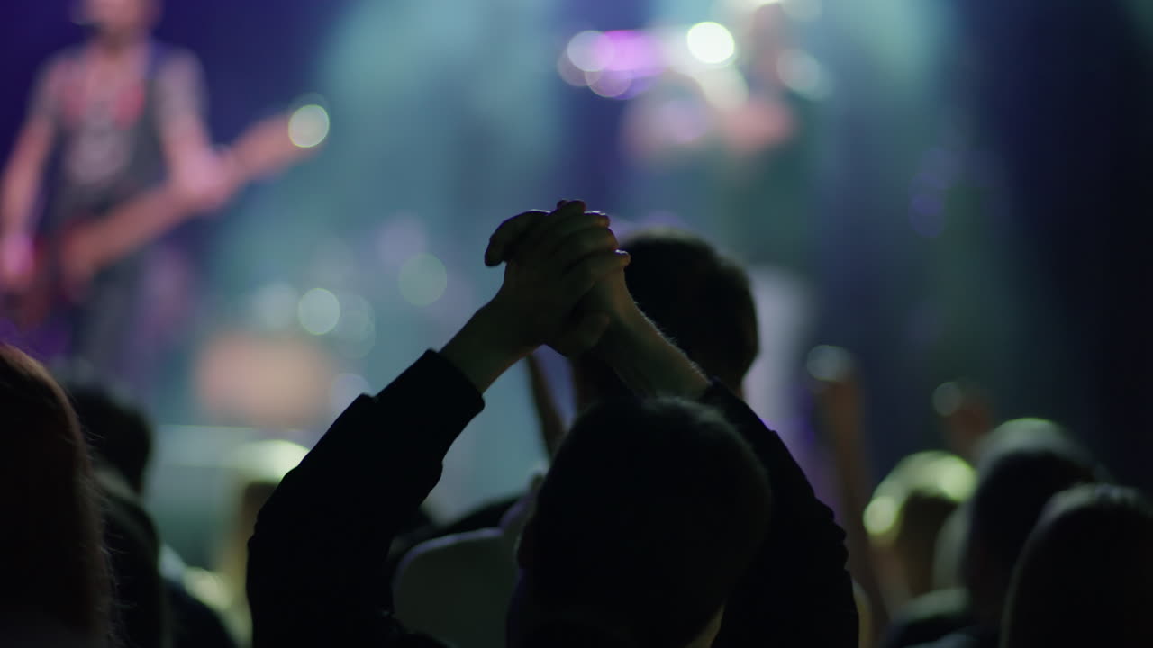 Fan che applaude con le mani sopra la testa con due artisti sfocati sul palco