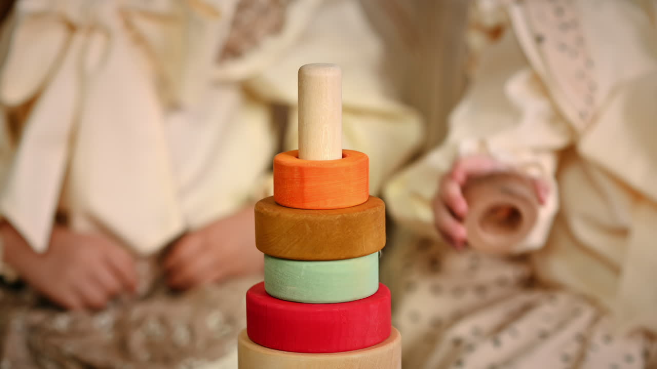 Two little girls playing with vibrantly colored blocks of a large wooden pyramid. Ecological and sustainability concept