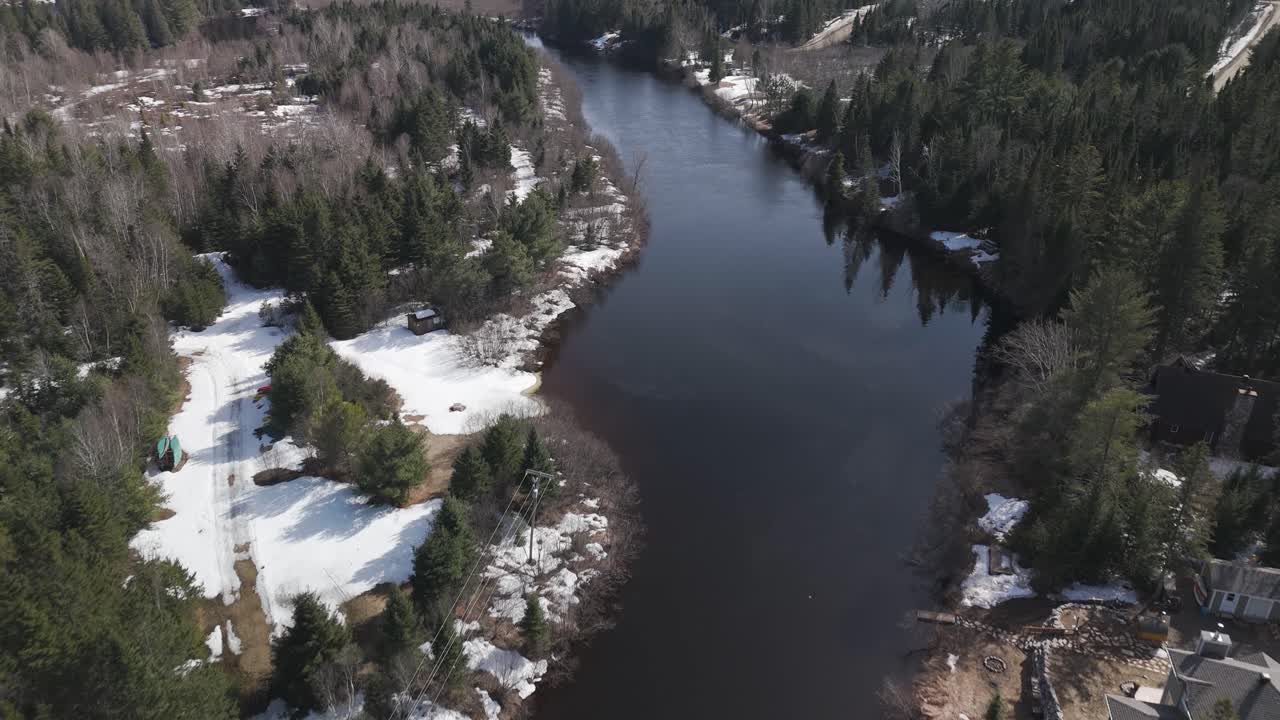Drone lentää joen yllä lumisten mäntymetsien keskellä Saint-Cômessa, joka on kunta Lanaudièren alueella Quebecissä, Kanadassa.