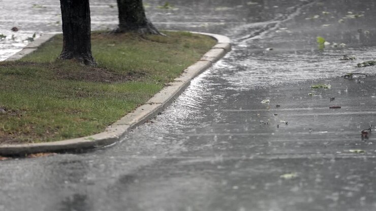 Rainfall splashing on asphalt road adjacent to grassy curb