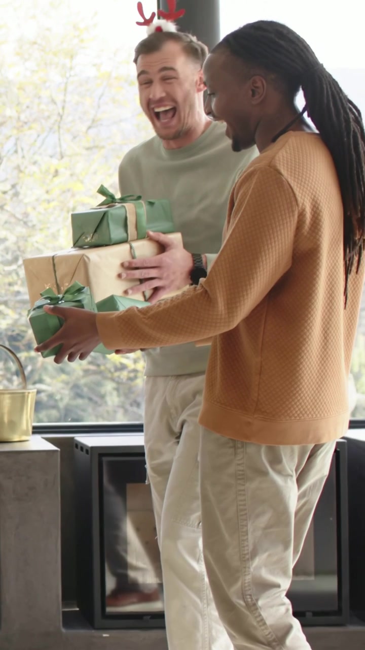 Video verticale: Entrano due uomini con maglia verde e maglione color cammello, portando regali al focolare