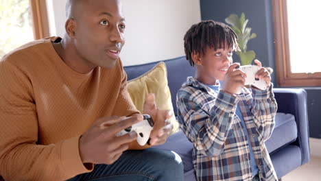 african american father and son playing video games at home, slow motion