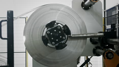 side shot of a roll of sheet metal being pulled off in an automated car parts factory