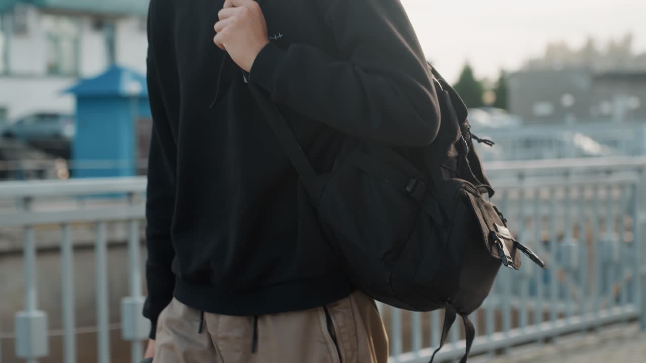 Viajante matinal em ponte da cidade. Homem com mochila caminha firmemente por uma ponte urbana ao amanhecer. Um indivíduo determinado com alça de câmera atravessa a ponte da cidade durante o nascer do sol com passos firmes.