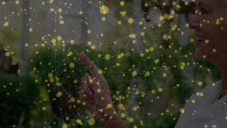 senior woman touching virtual nodes in garden, presenting digital network with glowing overlay