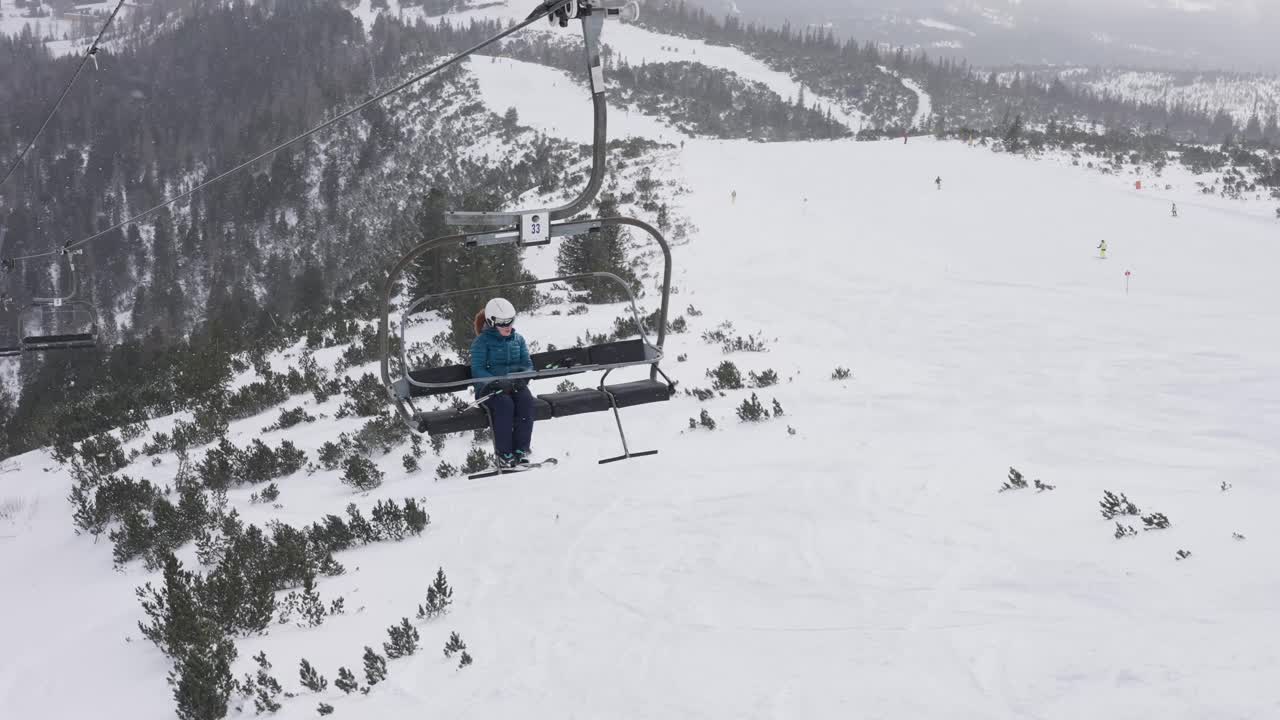 리프트를 타고 산을 오르는 여인 뒤로 눈 덮인 겨울 풍경이 펼쳐진다