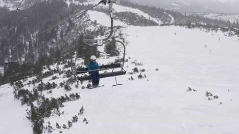 snowy winter landscape opens up behind a woman, who is going up the mountain on a lift