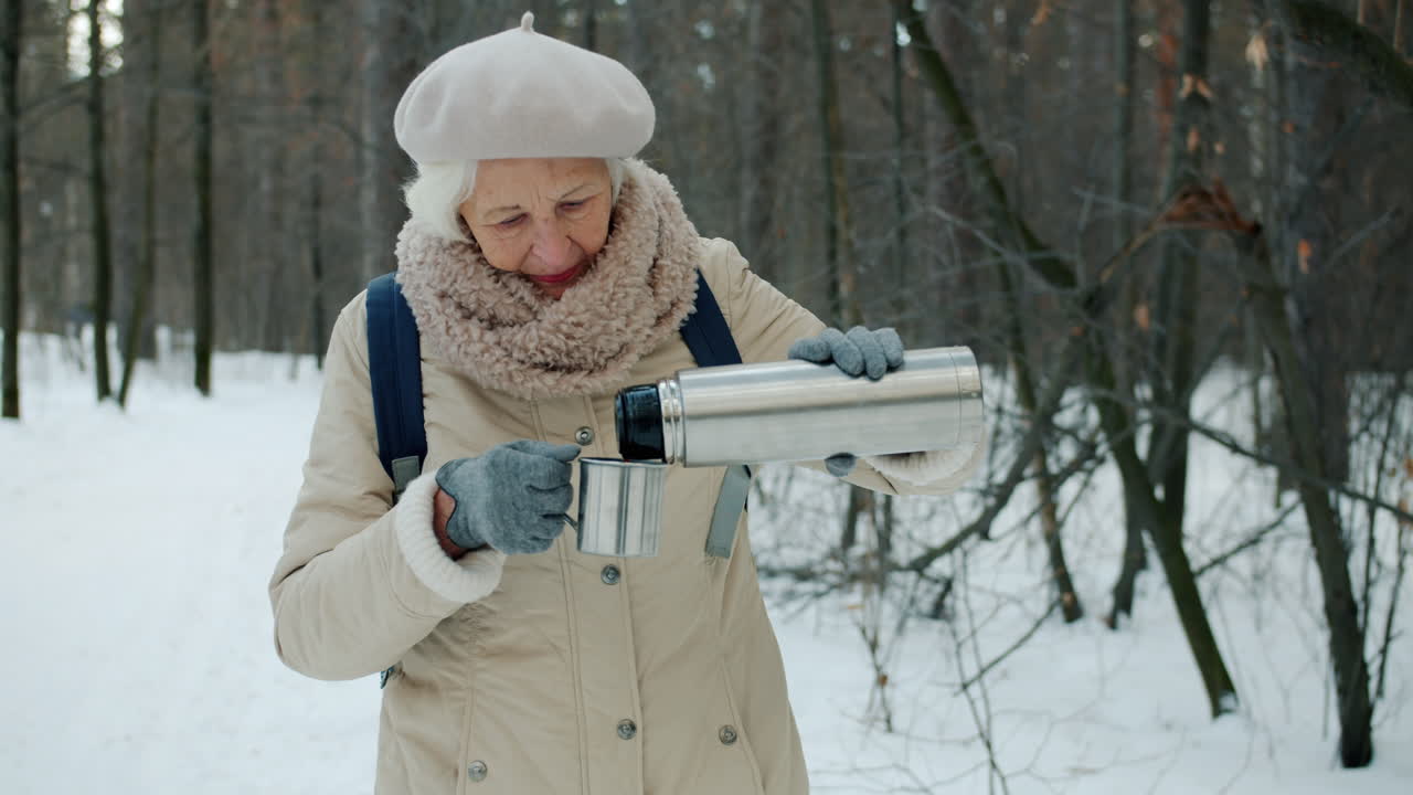 Senior Woman Hiking and Drinking Hot Tea in Winter Forest
