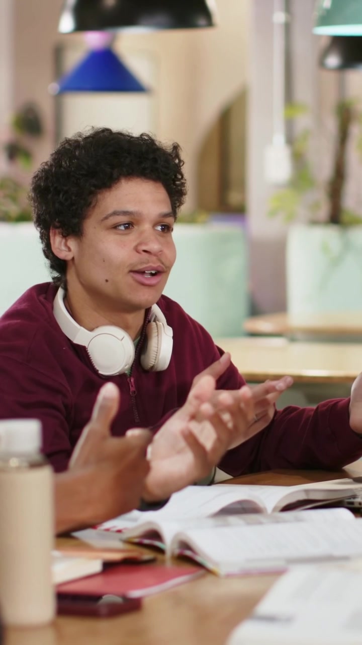 Vertical video: Answering peer prompt man in maroon sweatshirt gesturing at library with laptop