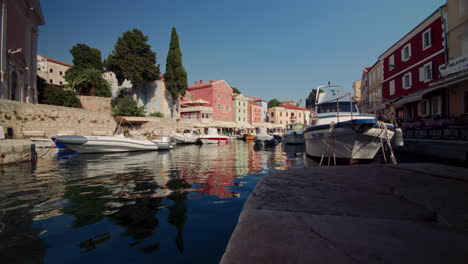 low angle view from stone docks of veli losinj looking out to boats anchored in shadow of buildings