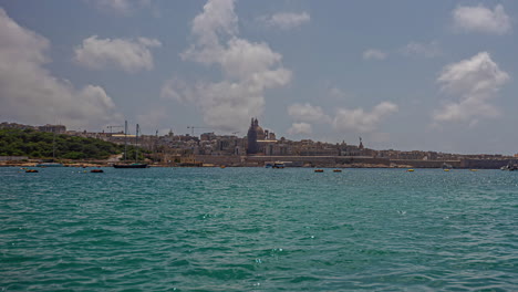 Zeitraffer-Vor-Der-Küste-Der-Wunderschönen-Stadt-Valletta-Auf-Der-Insel-Malta-Mit-Blick-Auf-Das-Türkisfarbene-Meer-Mit-Ruhigen-Wellen,-Schwimmenden-Segelschiffen-Und-Booten-Sowie-Den-Historischen-Gebäuden