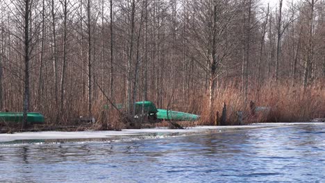 Upside-down-green-fishing-boats-parked-on-bare-tree-calm-lake-shore-with-ripples