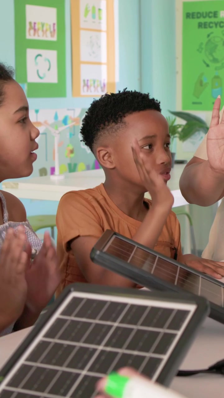 Vertical video: Pointing guide guiding boy in orange tee adjusting solar panel, seed tray in class