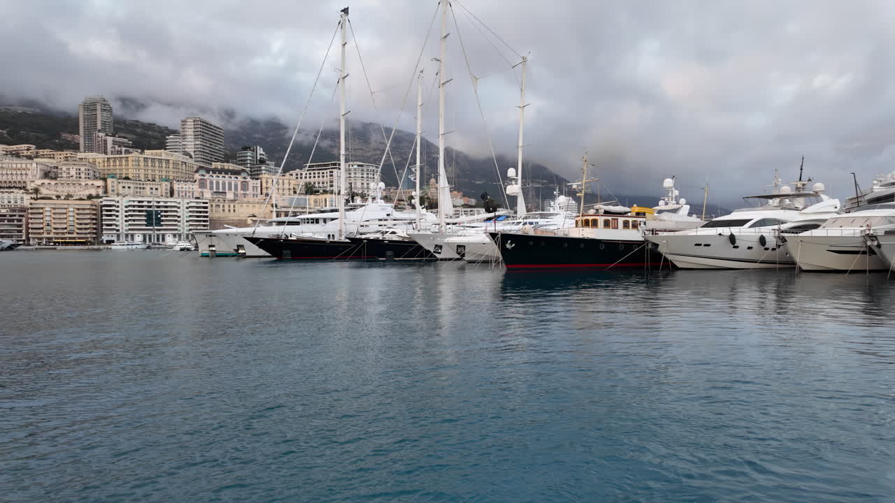 La Condamine, Monaco - 4 luglio 2025: fila di yacht di lusso ormeggiati a Port Hercules, con il paesaggio urbano di Monaco e le colline nebbiose sullo sfondo