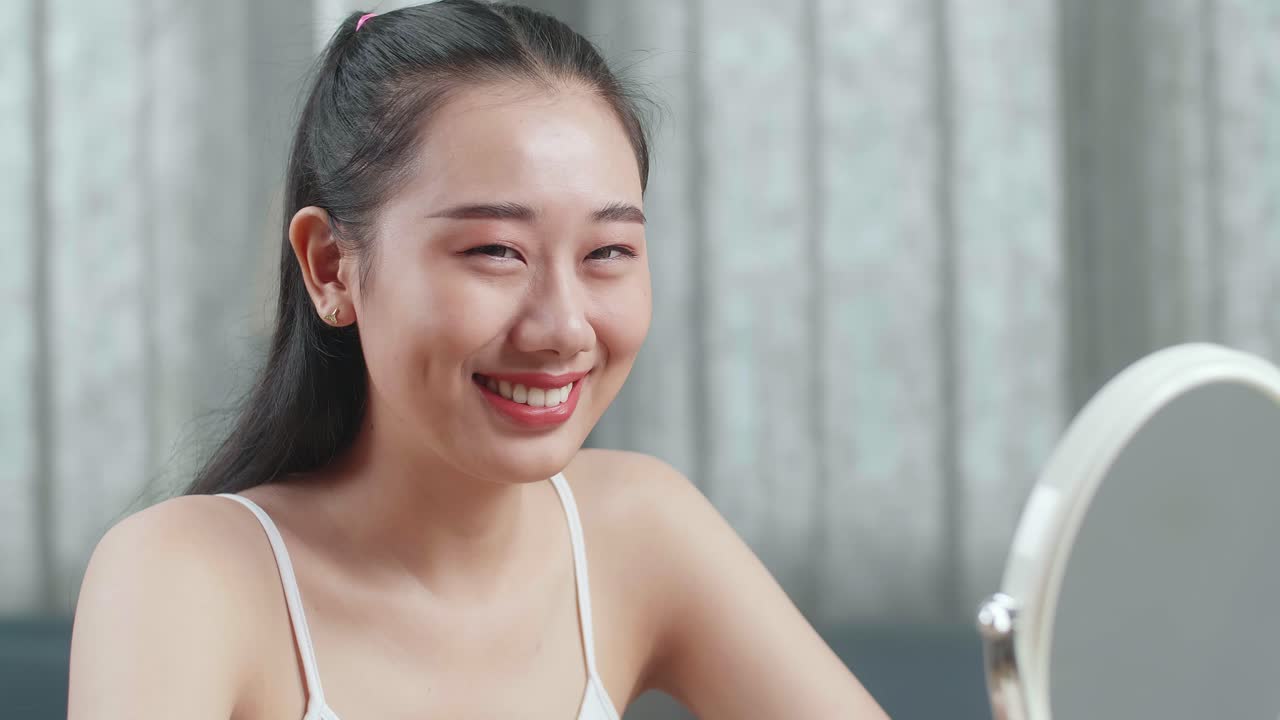 집에서 메이크업을 한 후 카메라에 미소 짓는 아름다운 젊은 아시아 여성의 클로즈업