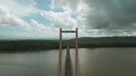 drone flying forwards through the hollow of a long gray bridge spanning a large south american river