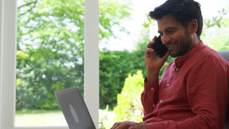 Man-Working-From-Home-Sitting-On-Floor-In-Lounge-Using-Laptop-And-Mobile-Phone