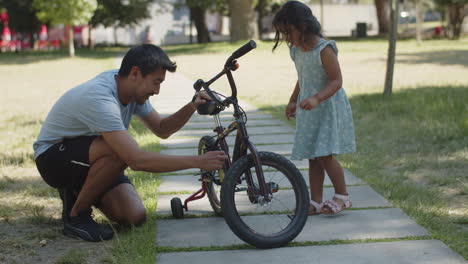 feliz padre ajustando la cadena en bicicleta de su pequeña hija