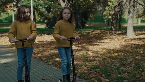 caucasian child siblings having fun in the woods while driving a push scooter.