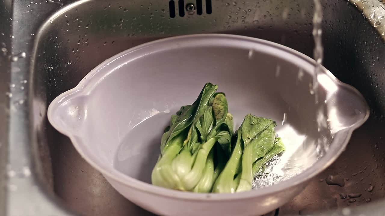 Hand turning on the faucet in the sink to soak wilted bok choy to avoid food loss and wastage for a sustainable ecological lifestyle