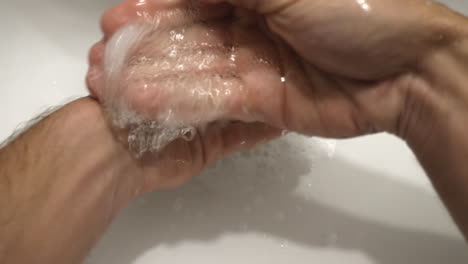 person's hand washing with soap under clean tap water from a faucet - to prevent corona virus - high-angle shot