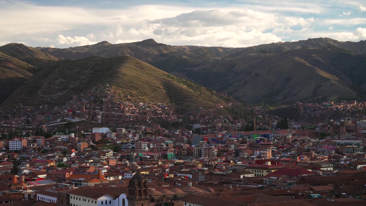 Cusco Panoramic Plaza de Armas main square city of Cuzco Peru cityscape landscape rainy season sunset golden hour clouds Peruvian neighborhood buildings on mountainside Anta Province Andes pan left