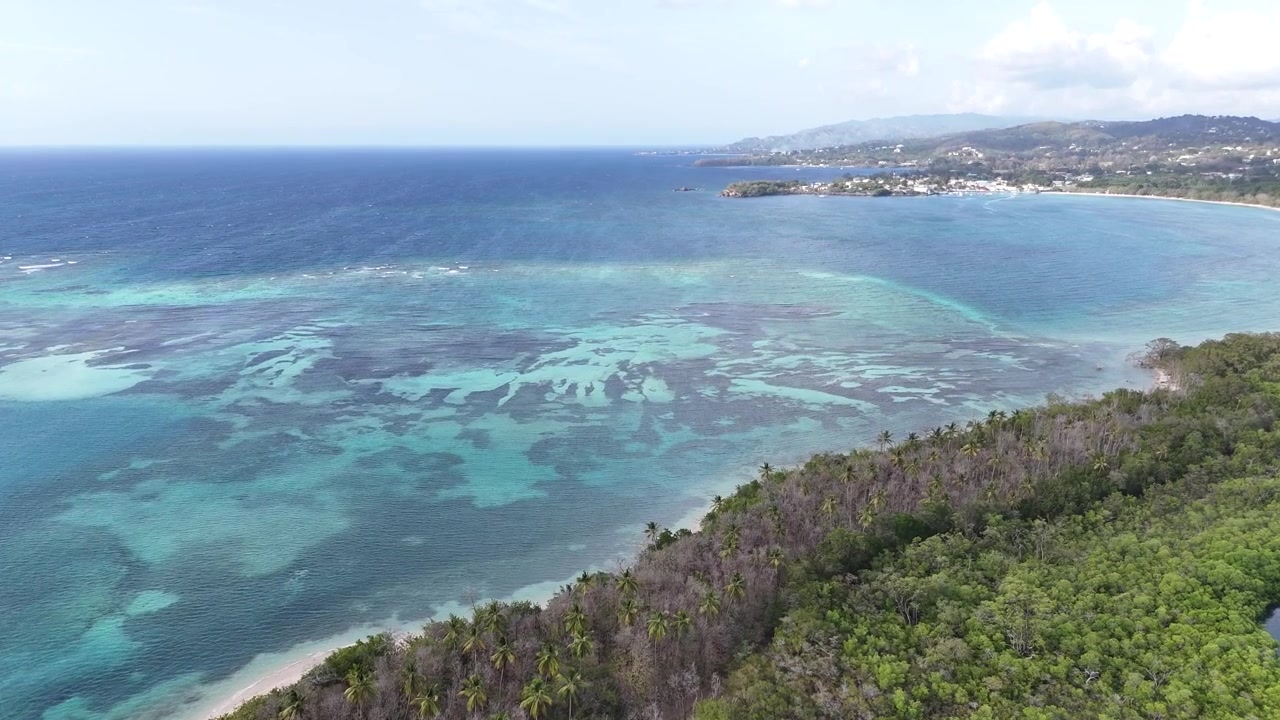 Ampia veduta aerea della barriera corallina e delle acque turchesi che circondano No Man's Land. Paesaggio costiero tropicale dell'isola di Tobago con mare cristallino e creste montuose distanti