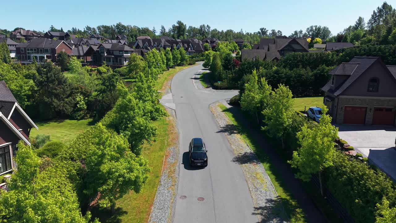 A luxury black SUV cruising on a luxury suburban neighborhood under a clear blue sky in Langley Township, Canada