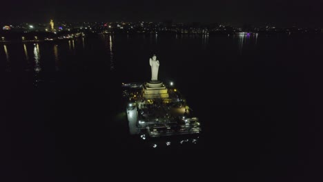 a cinematic aerial shot of hussain sagar lake, hyderabad's most well-known landmark, at night indian monolith known as the buddha statue of hyderabad