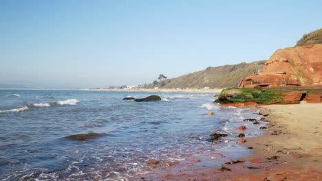 Wide-shot-of-sea-waves-rolling-in-over-small-cutoff-beach-overlooking-the-larger-Exmouth-beach,-East-Devon,-UK