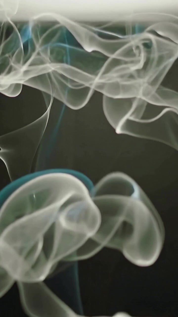 Vertical video: Rising thin smoke puffs curling in studio after wisps enter with soft light band