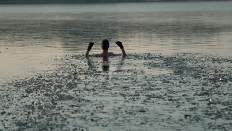 Young-man-with-a-hand-gloves-and-swim-wear-walking-into-deep-frozen-lake