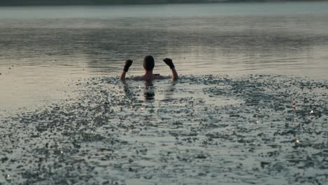 joven con guantes de mano y ropa de baño caminando hacia un lago congelado