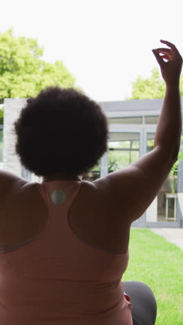 video of back of plus size african american woman exercising at home, practicing yoga