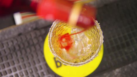 pouring red syrup into a glass filled with ice at the bottom to prepare cocktail in a bar slow motion