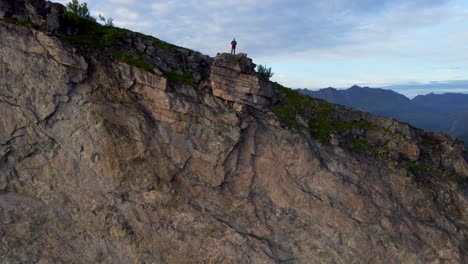 hiker standing on the edge of a steep cliff during summer on the hiking trail to hesten, senja island