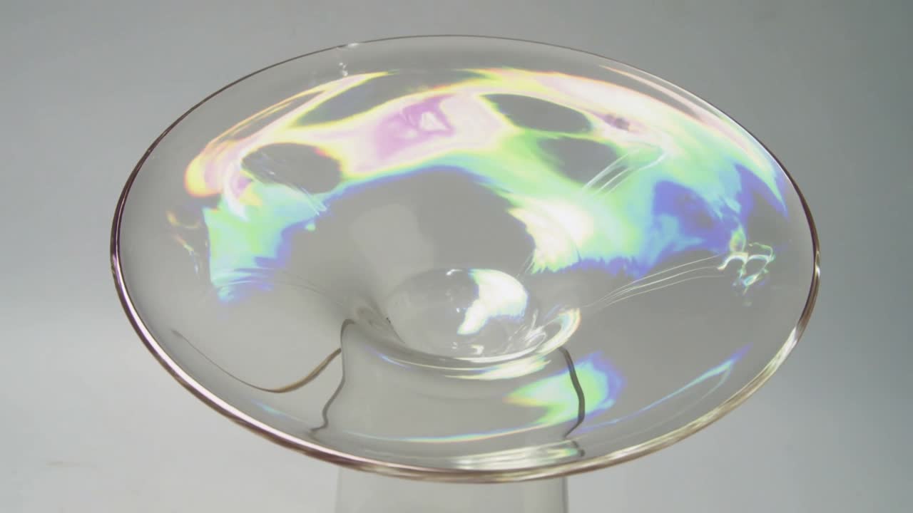 Showing clear membrane forming shifting colors on studio pedestal under light causing red dot