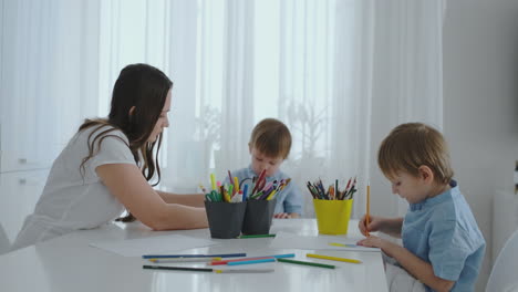 mom helps sons learn to draw doing homework preschool preparation at home sitting in the white kitchen.
